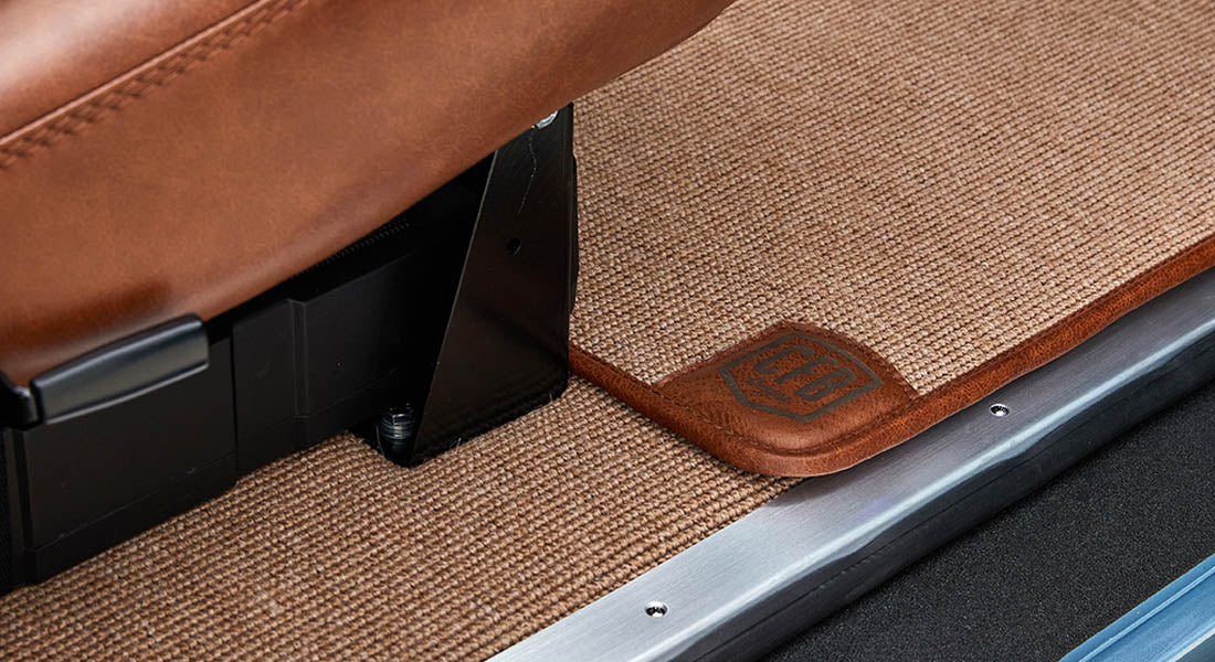 Brown textured carpet floor mat with leather trim and embossed 'CGA' logo inside Classic Ford Bronco