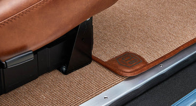 Brown textured carpet floor mat with leather trim and embossed 'CGA' logo inside Classic Ford Bronco