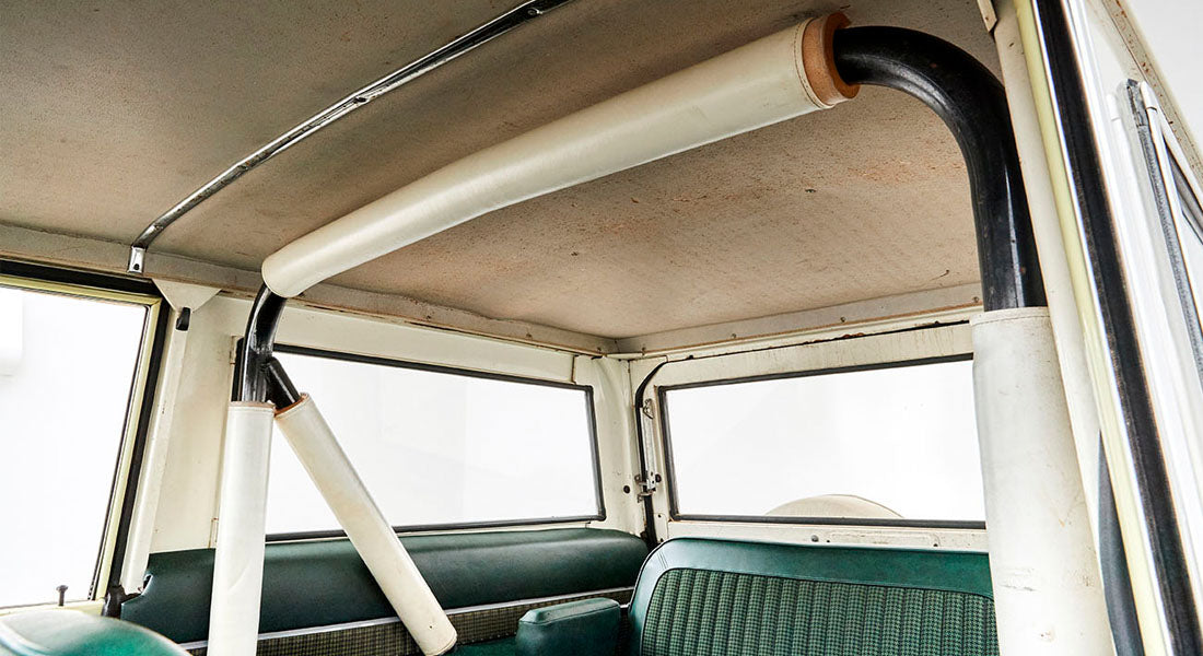 Black and white roll cage structure inside Classic Ford Bronco with green seats and beige ceiling