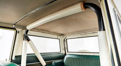 Black and white roll cage structure inside Classic Ford Bronco with green seats and beige ceiling