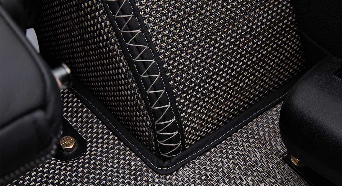 Close-up of woven carpet with black leather trim and white stitching