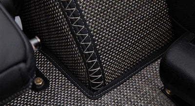 Close-up of woven carpet with black leather trim and white stitching