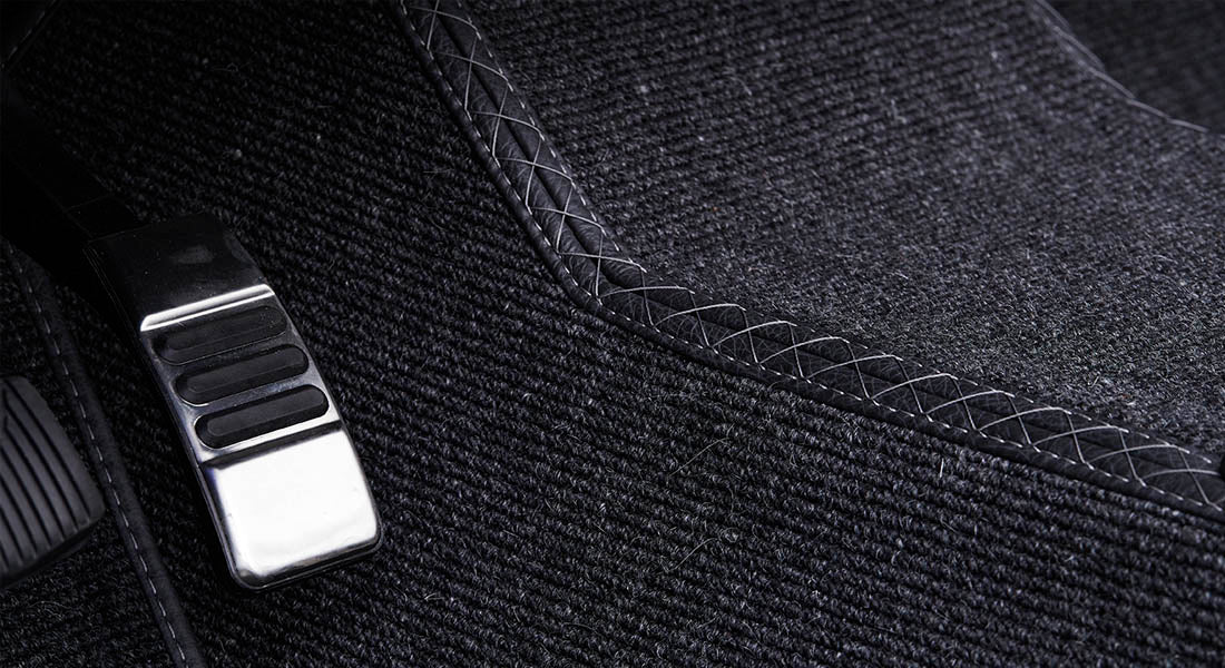 Black textured carpet inside vehicle with stitched edging detail
