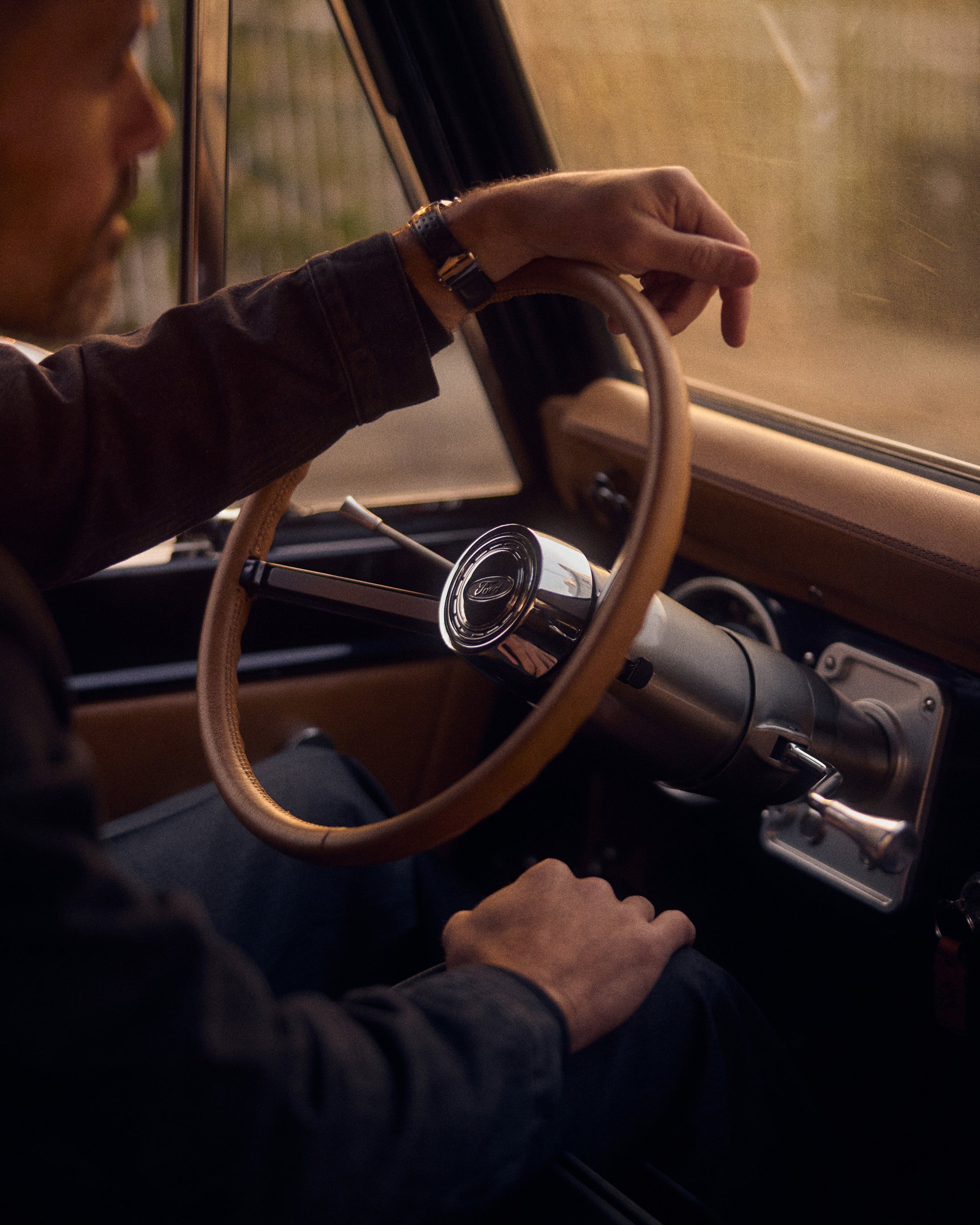Man's hand on tan steering wheel inside Classic Ford Bronco