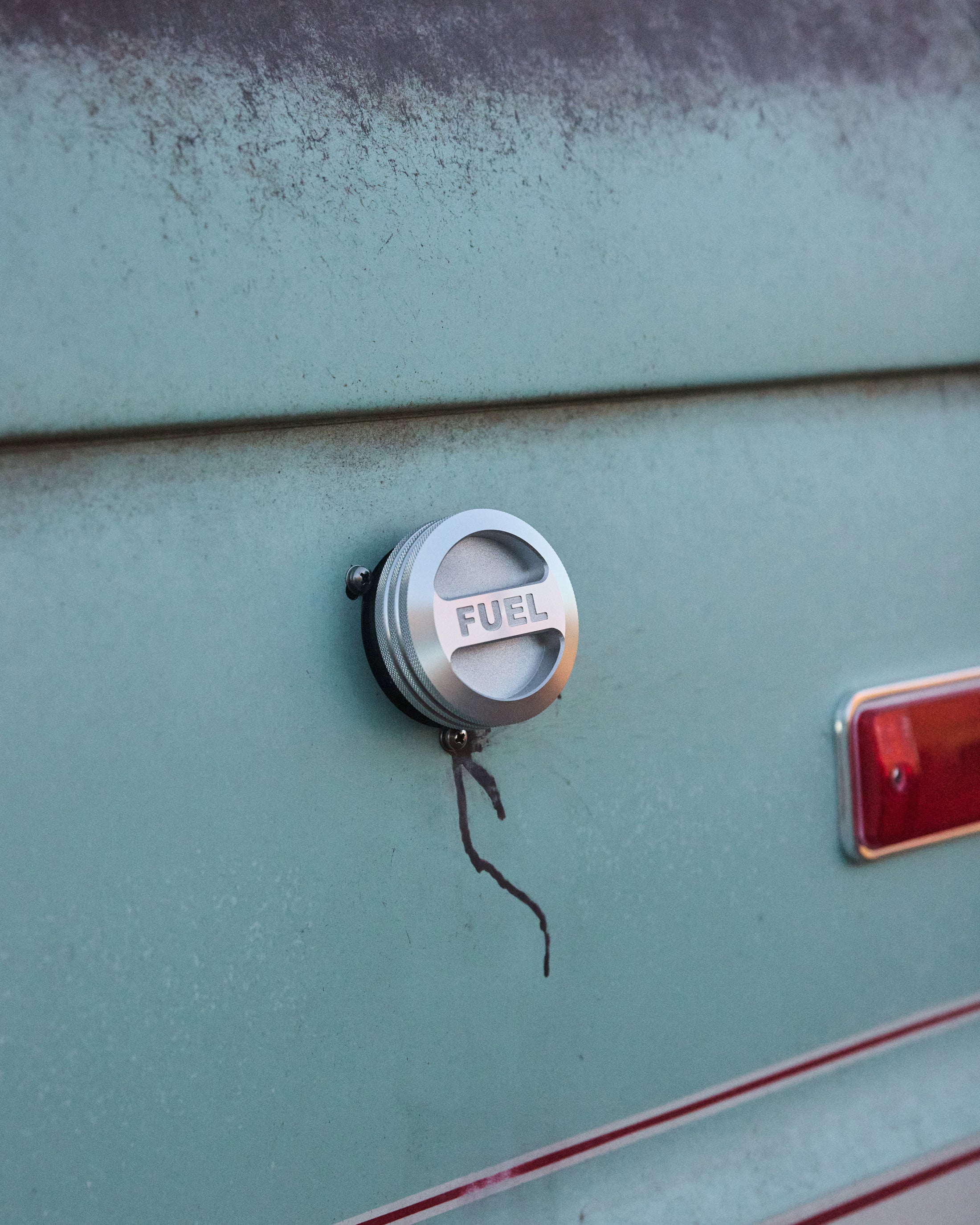 Close-up of a silver fuel cap on a faded turquoise vehicle exterior