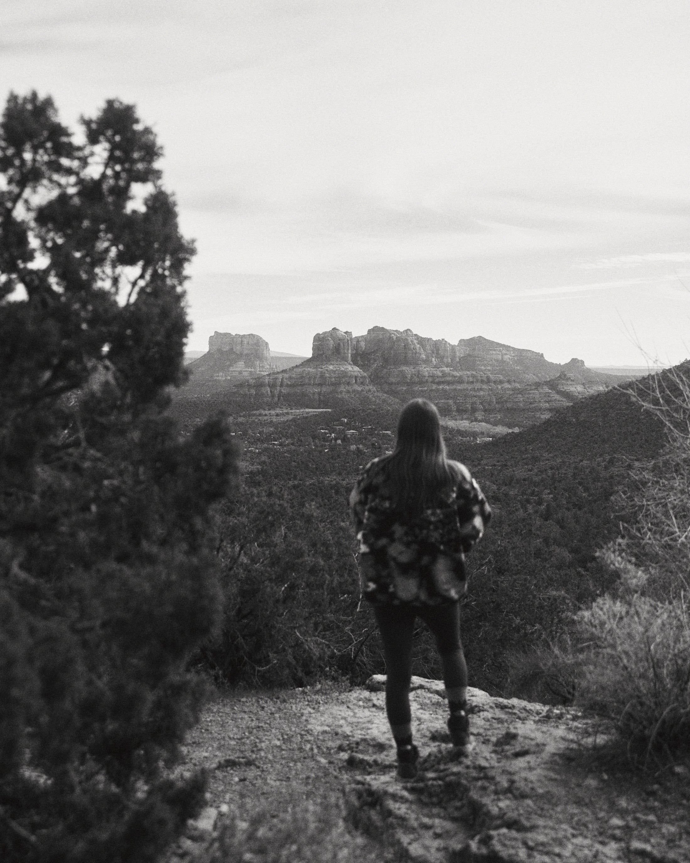 Person standing on a hill overlooking a vast hilly landscape with rock formations in black and white