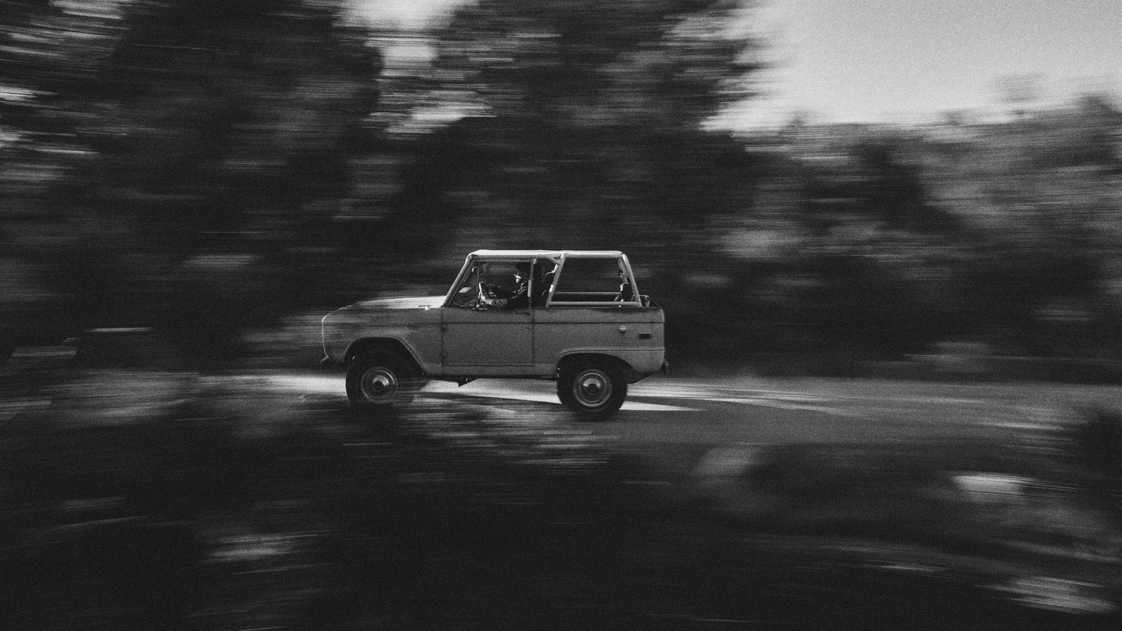 Black and white motion blur view of a Classic Ford Bronco driving with a driver visible
