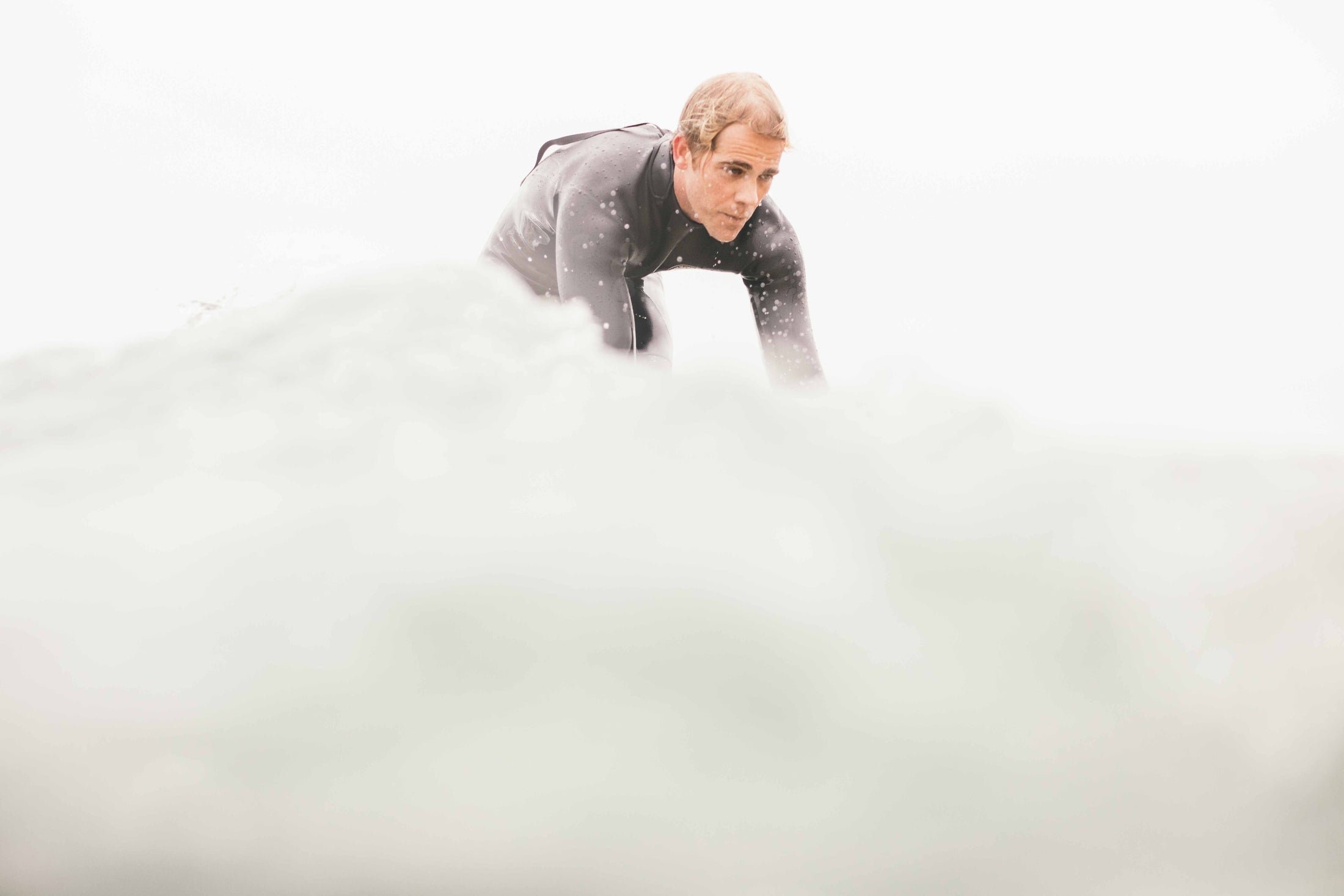 Man in wetsuit crouching in ocean water with waves splashing