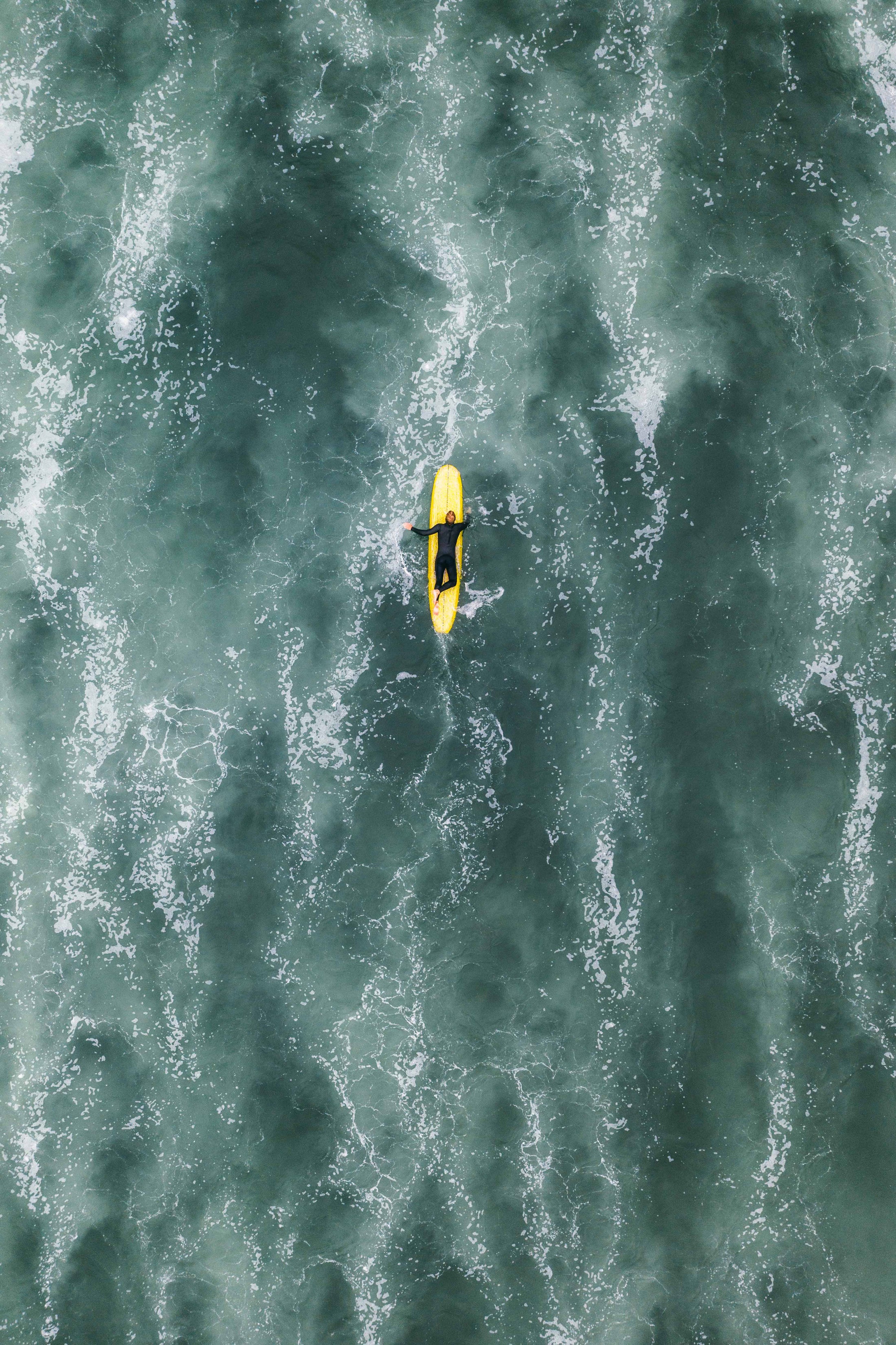 Aerial view of person floating on yellow surfboard in ocean water