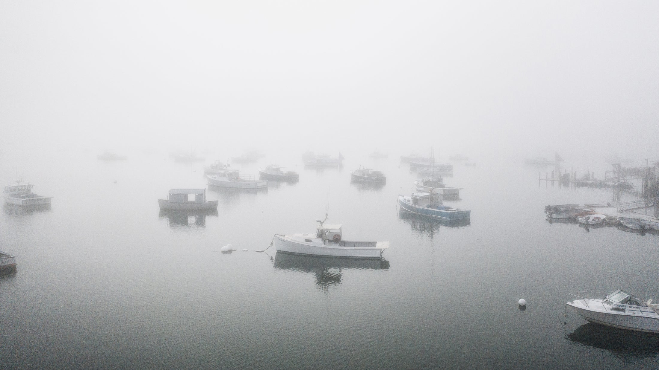 Multiple boats moored in calm water surrounded by thick fog.