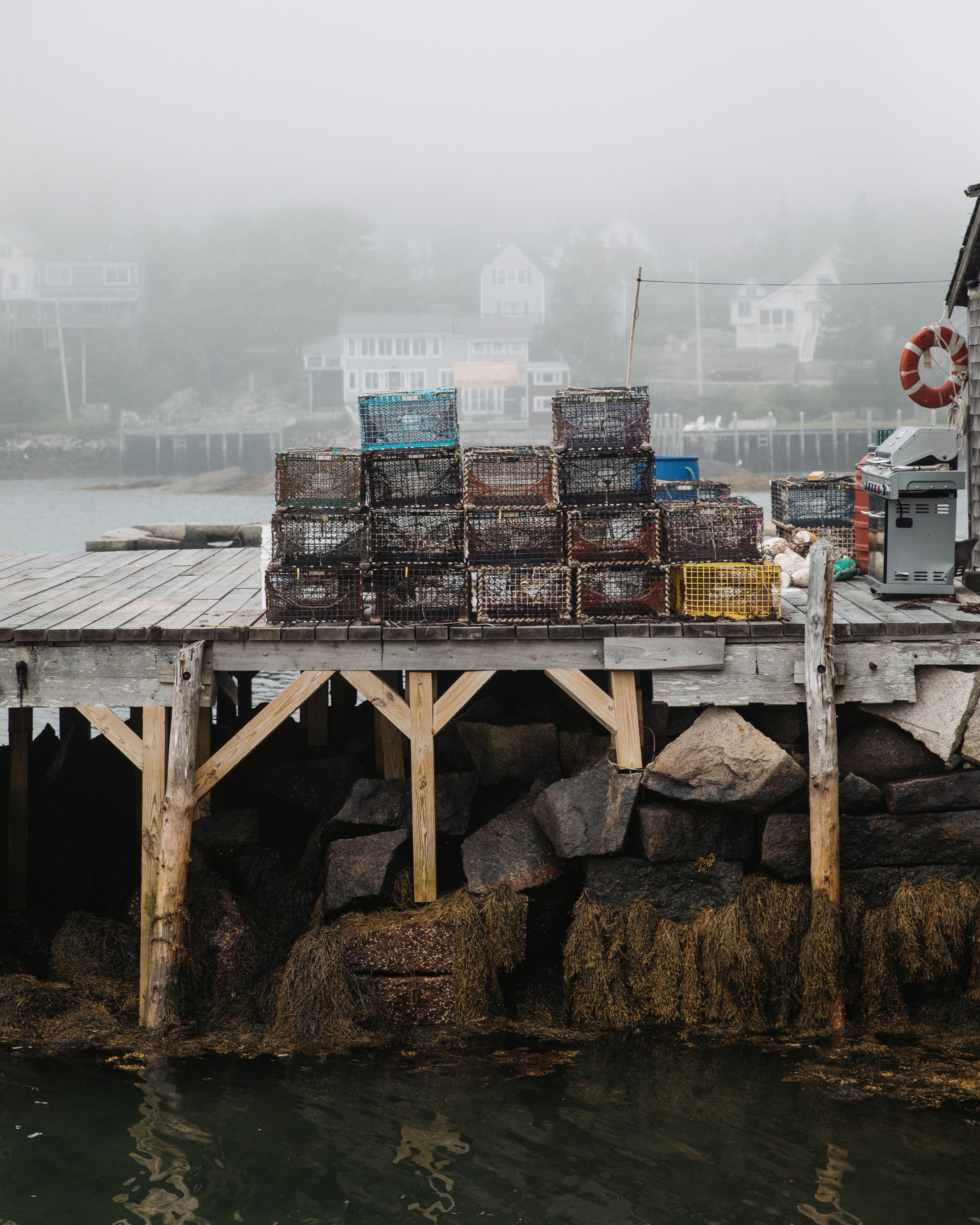 Stacked lobster traps on a foggy wooden dock over rocky shoreline