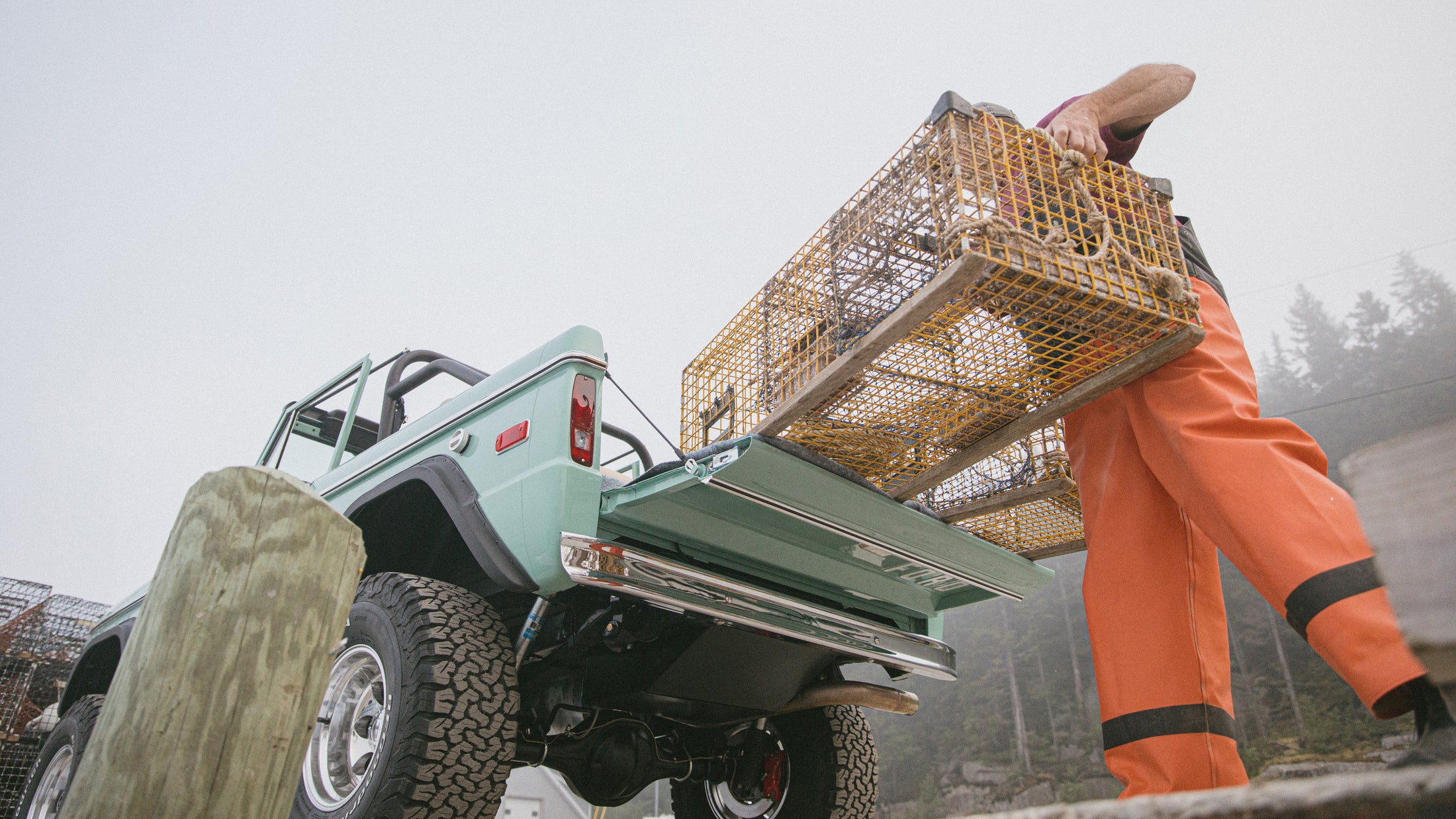 Classic Ford Bronco light green with open tailgate loaded with lobster traps at harbor in foggy weather