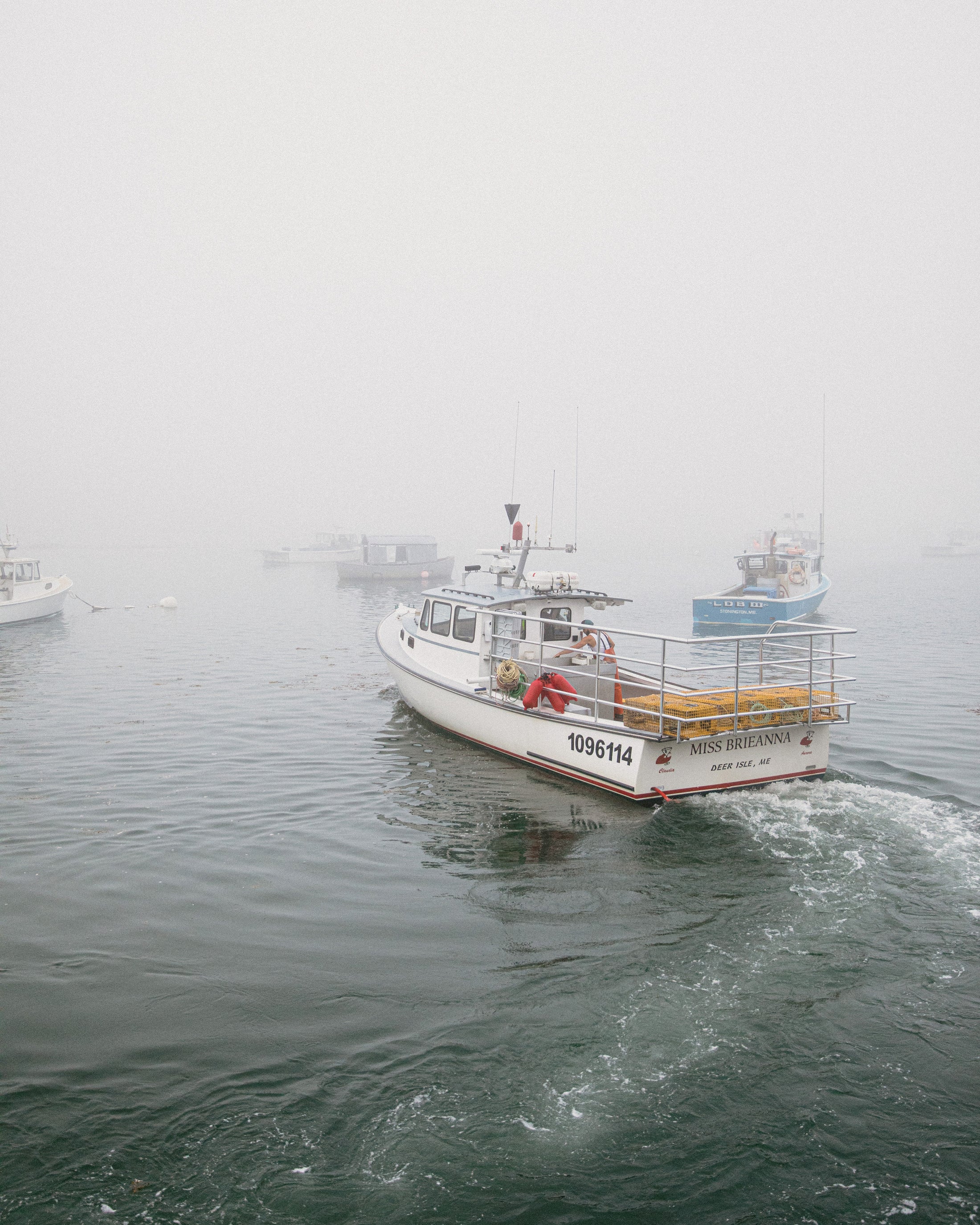 Fishing boat named Miss Brieanna moving through foggy water with other boats nearby.