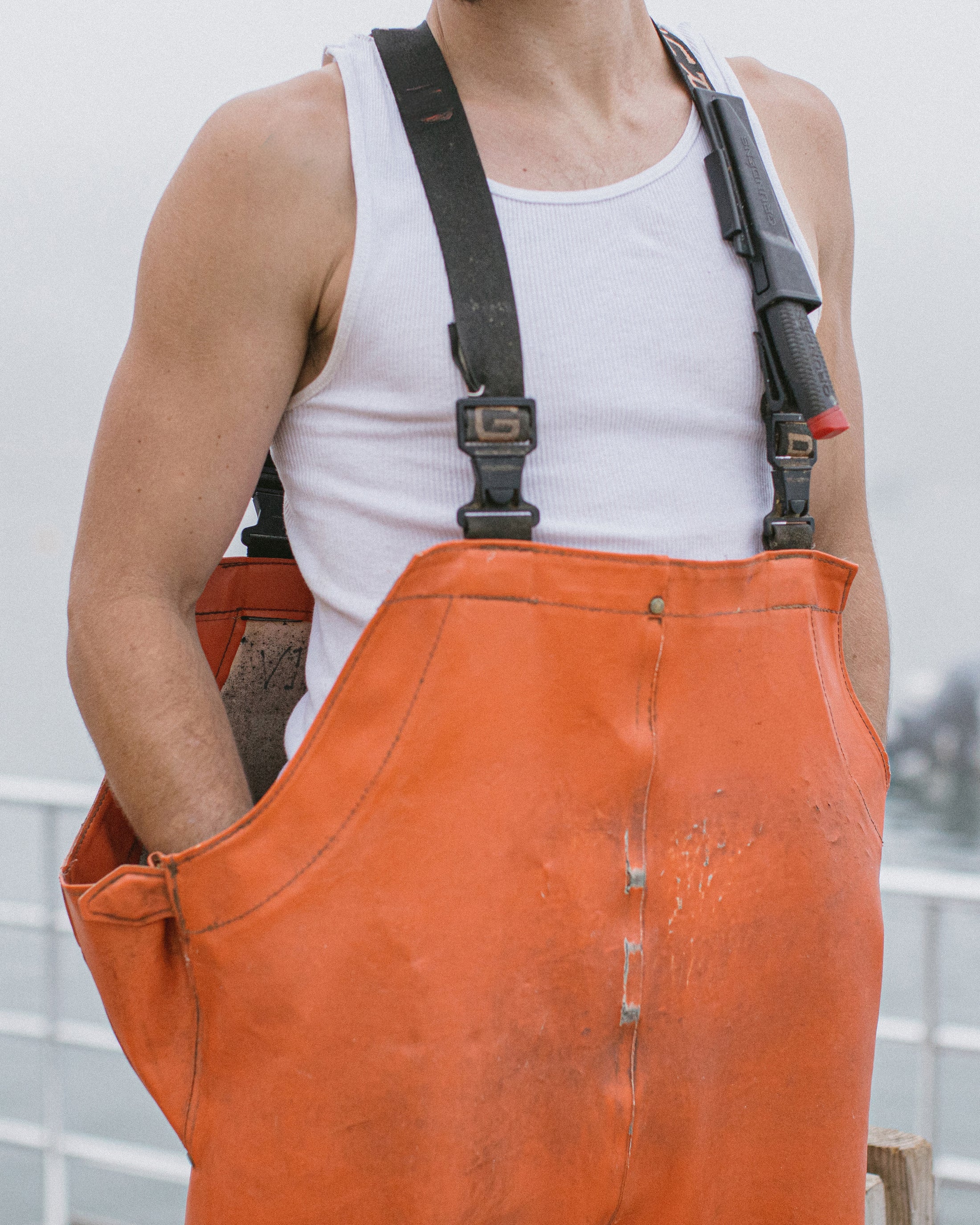 Person wearing white tank top and orange bib pants with hands in pockets