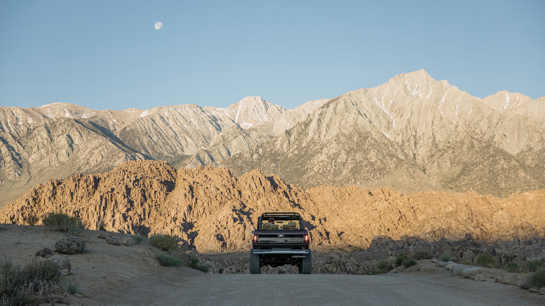 Rear view of Classic Ford Bronco parked on dirt road facing vast rocky mountain range
