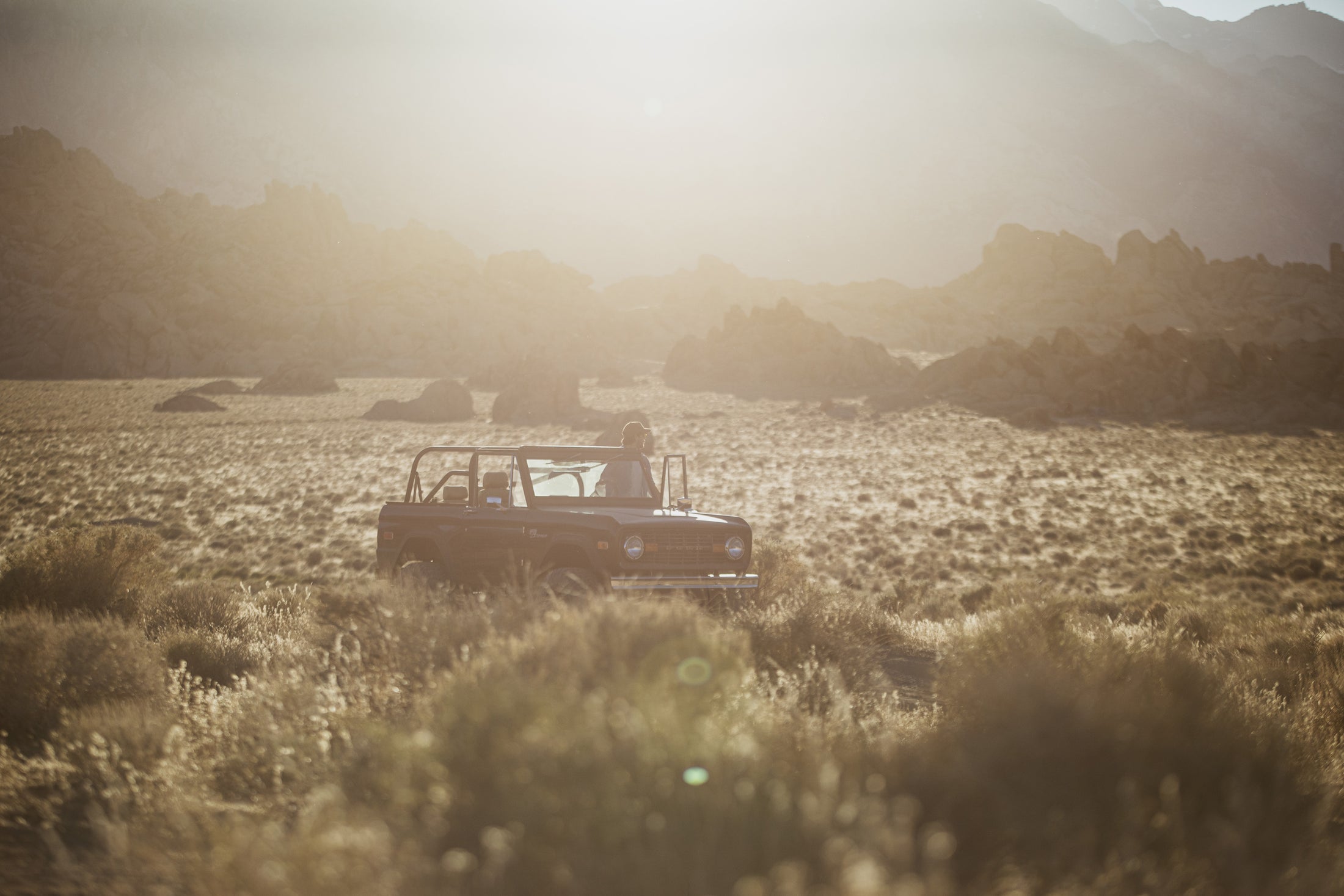 Classic Ford Bronco with open doors in a sunlit desert valley surrounded by rocky hills