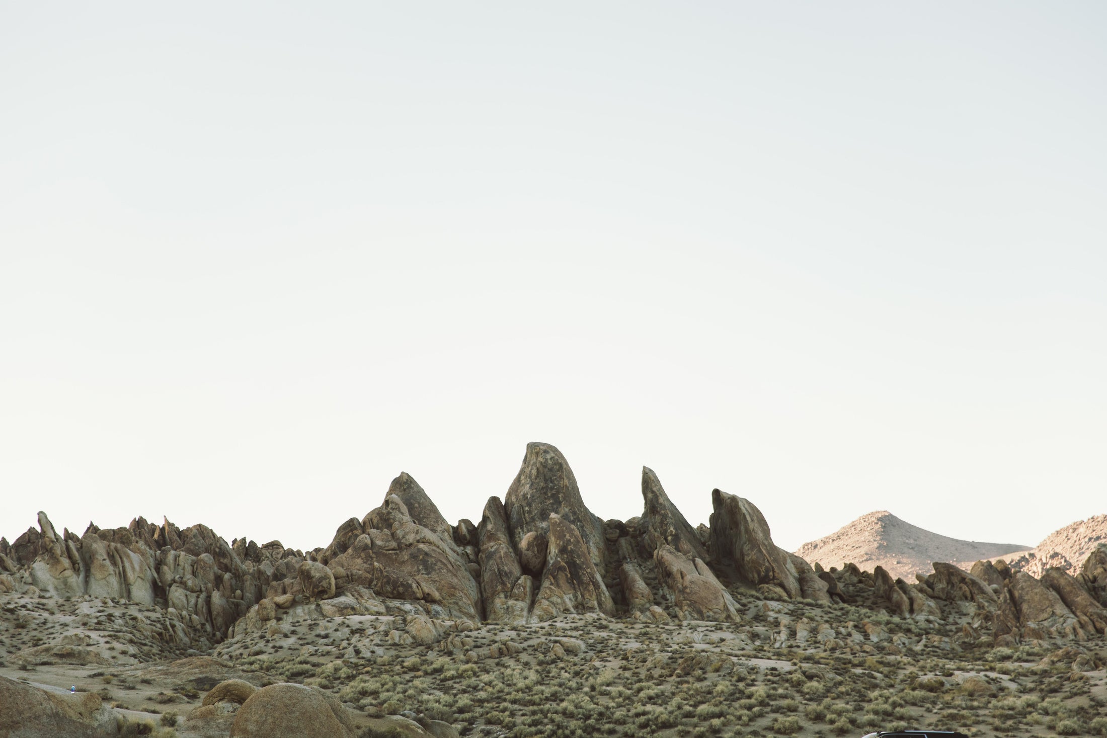 Rocky mountain landscape under a pale sky with sunlit rugged peaks and sparse desert vegetation