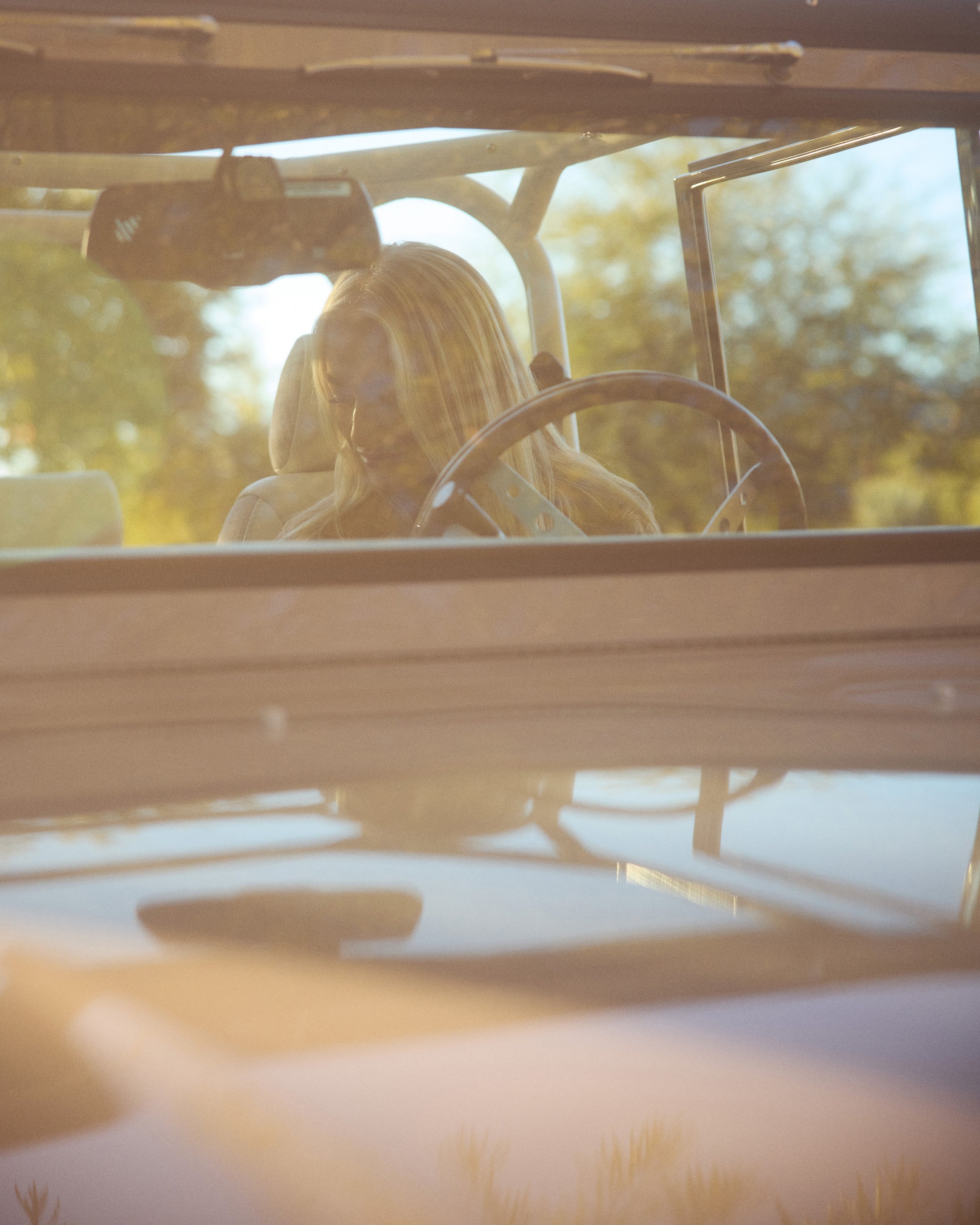 Woman sitting inside a Classic Ford Bronco, visible through the windshield