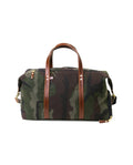Camouflage duffel bag with brown leather handles and straps on a white background