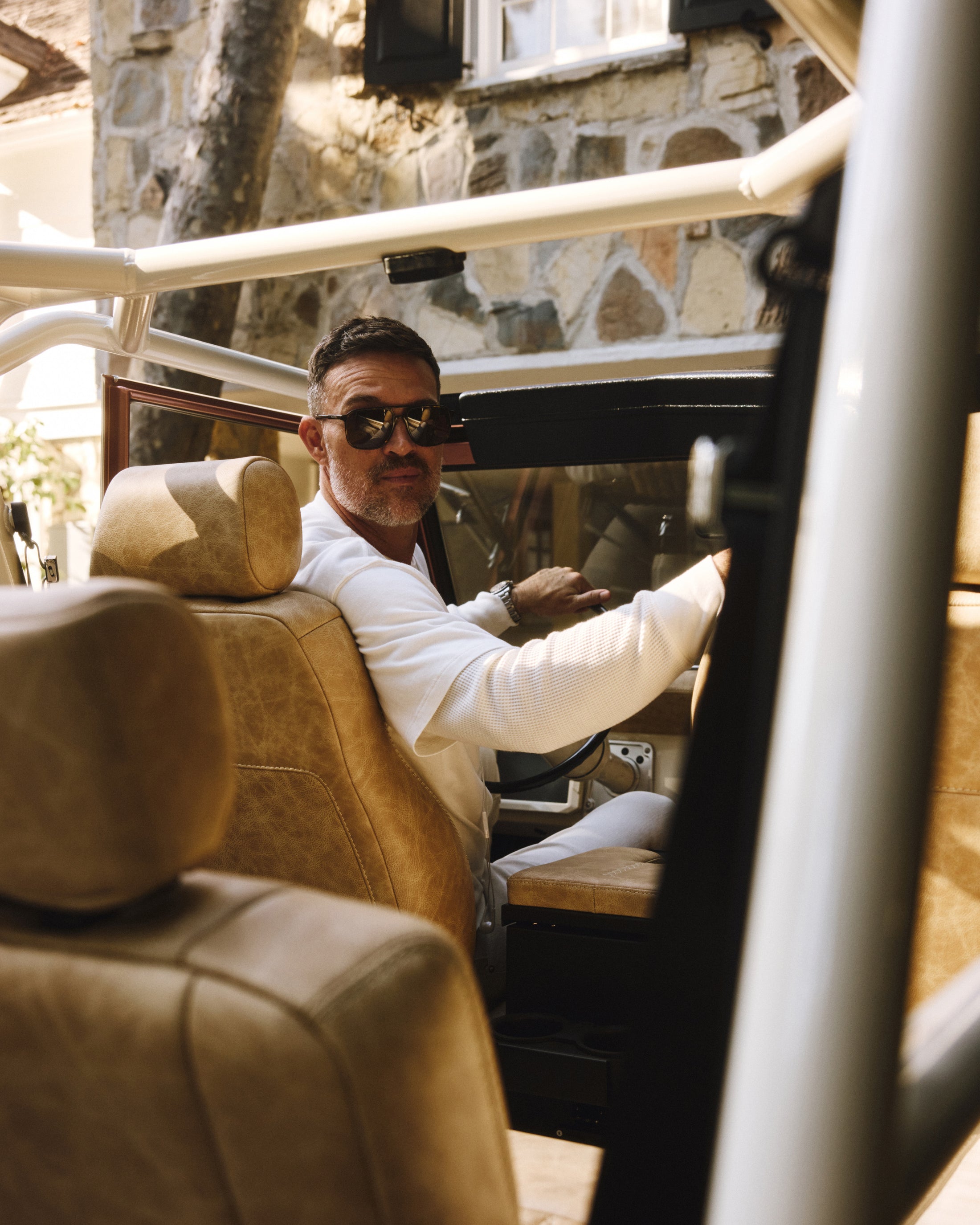 Man in sunglasses sitting in the driver seat of a Classic Ford Bronco with tan interior