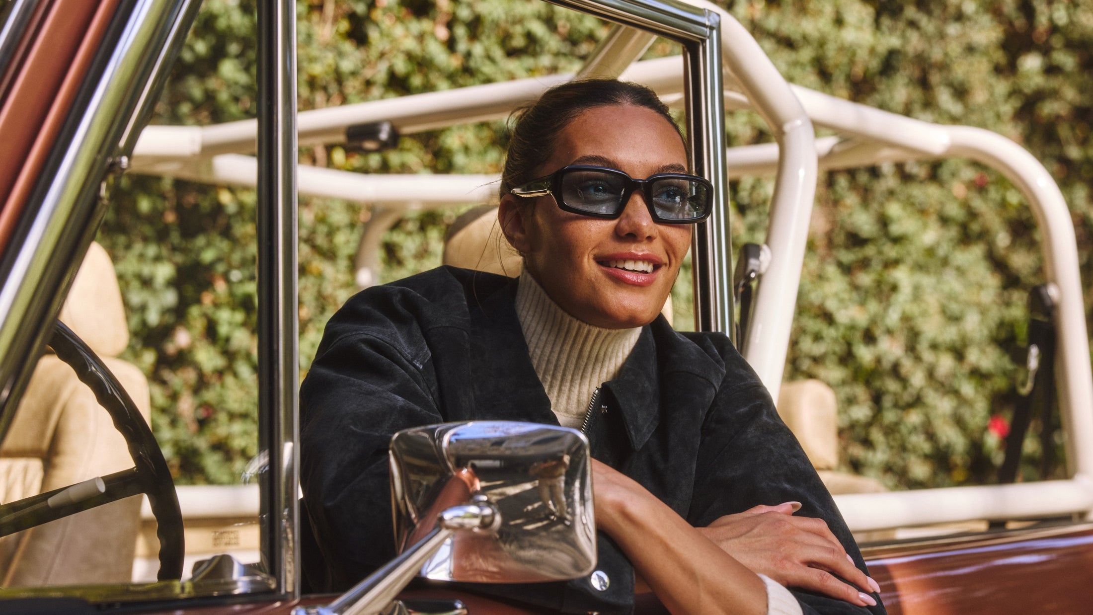 Woman with dark sunglasses leaning on the door of a Classic Ford Bronco with tan seats