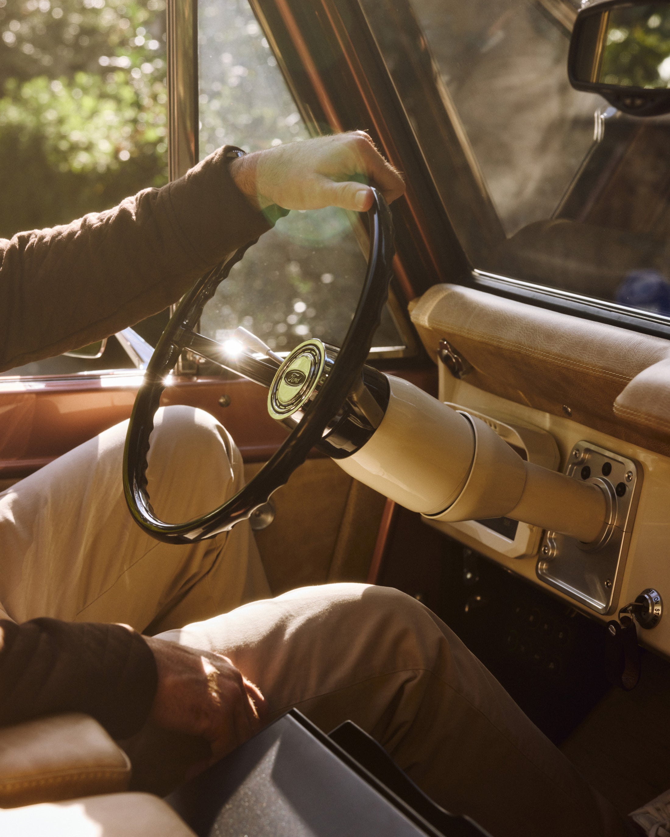 Classic Ford Bronco steering wheel and dashboard with a person holding the wheel in warm sunlight.