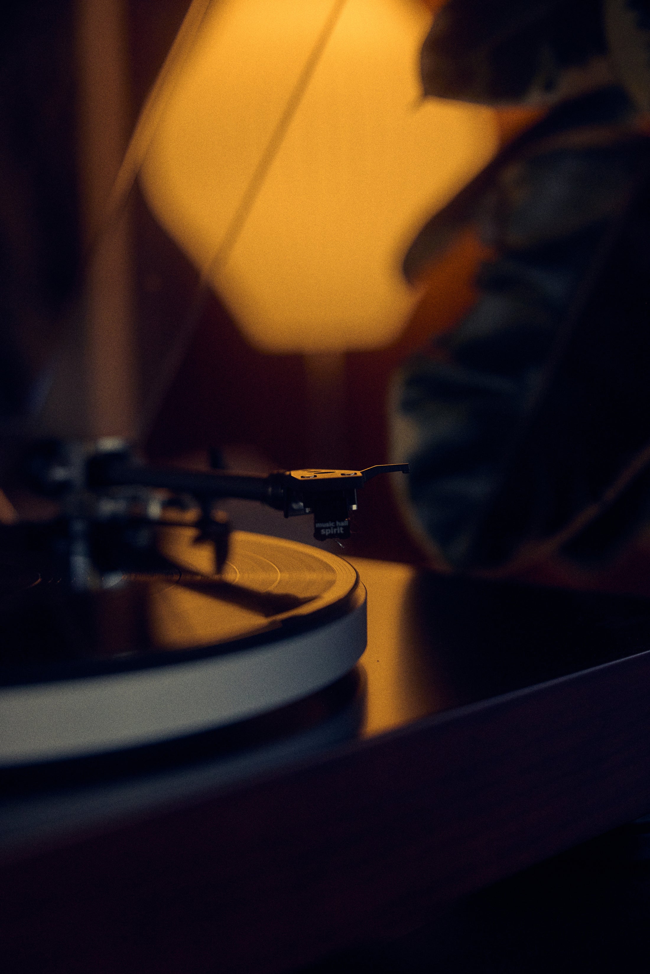 Close-up of a turntable needle on a spinning vinyl record with warm lamp light in background.