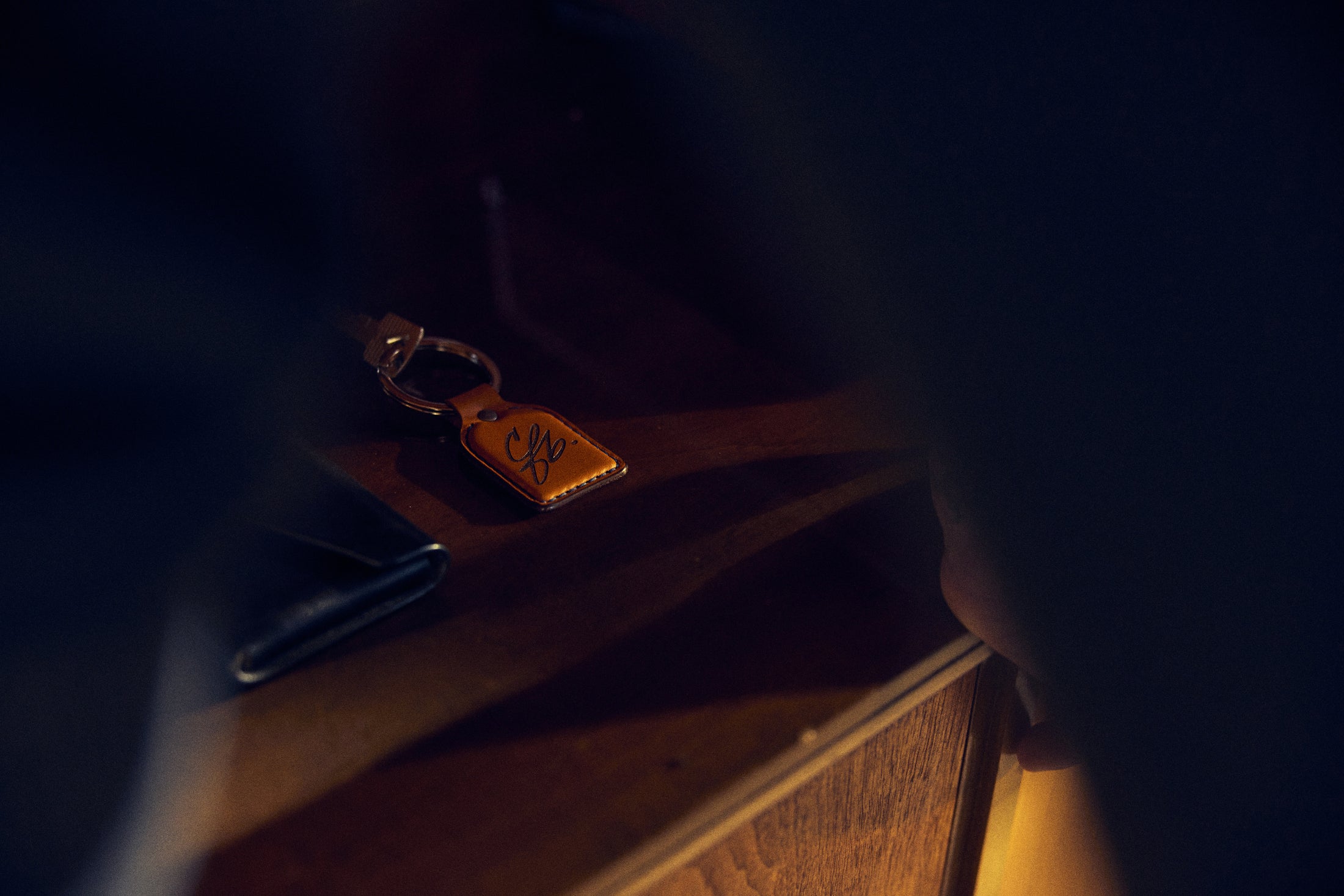 Bronze keychain with initials on a wooden surface inside a vehicle interior.