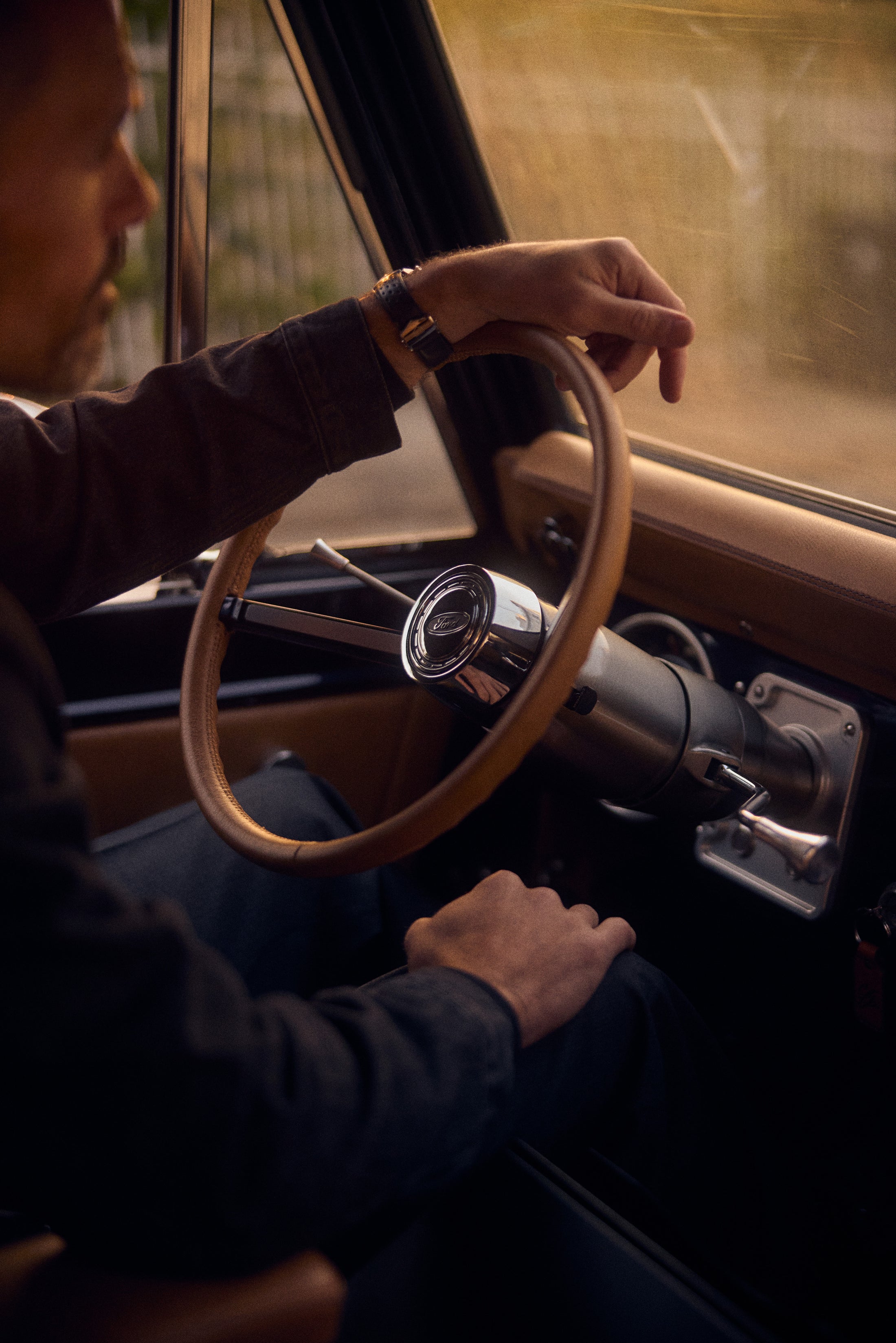 Man resting his arm on a steering wheel of a Classic Ford Bronco bathed in warm sunlight.
