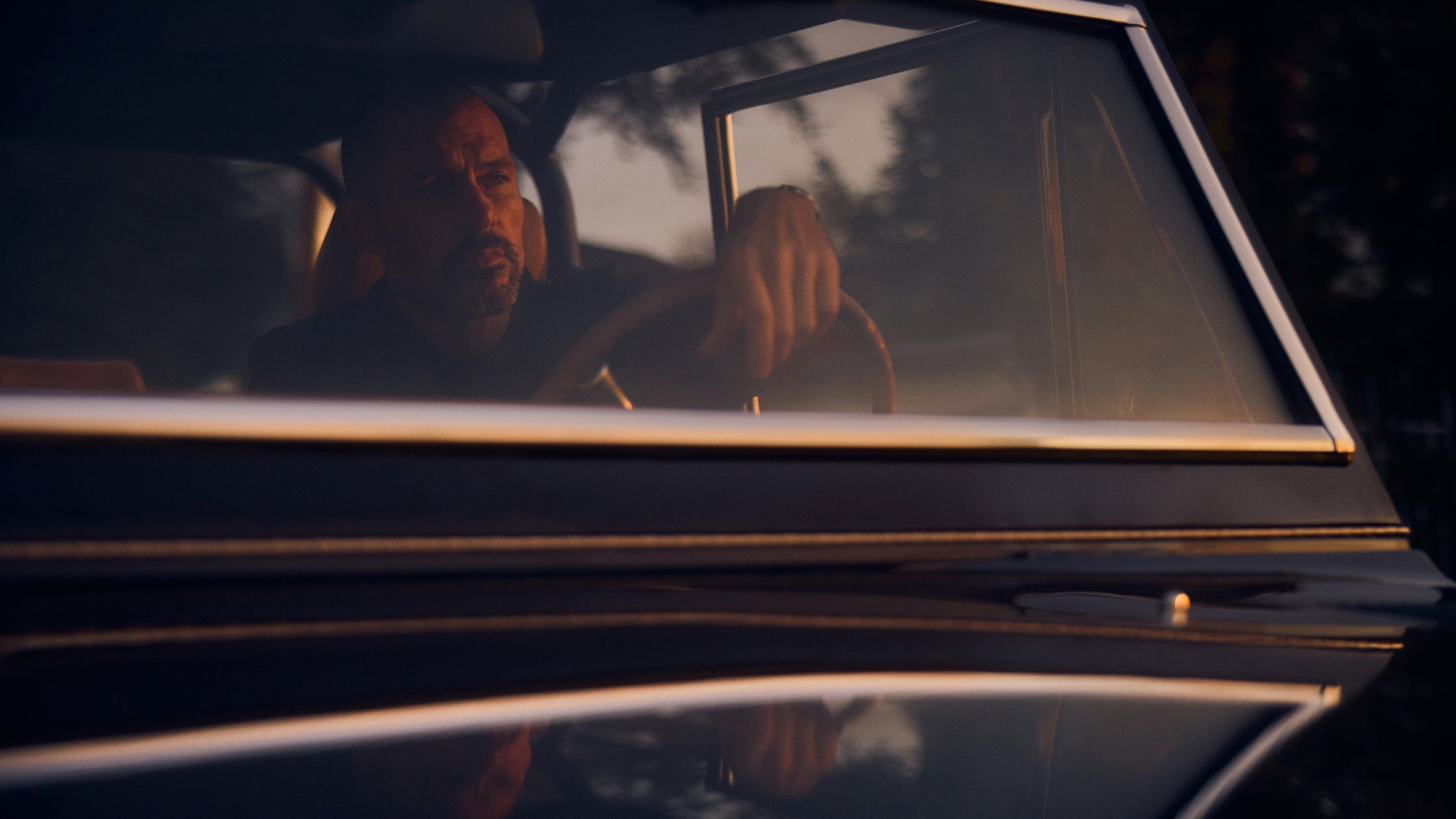 Man seated inside a Classic Ford Bronco, visible through the window, at dusk.