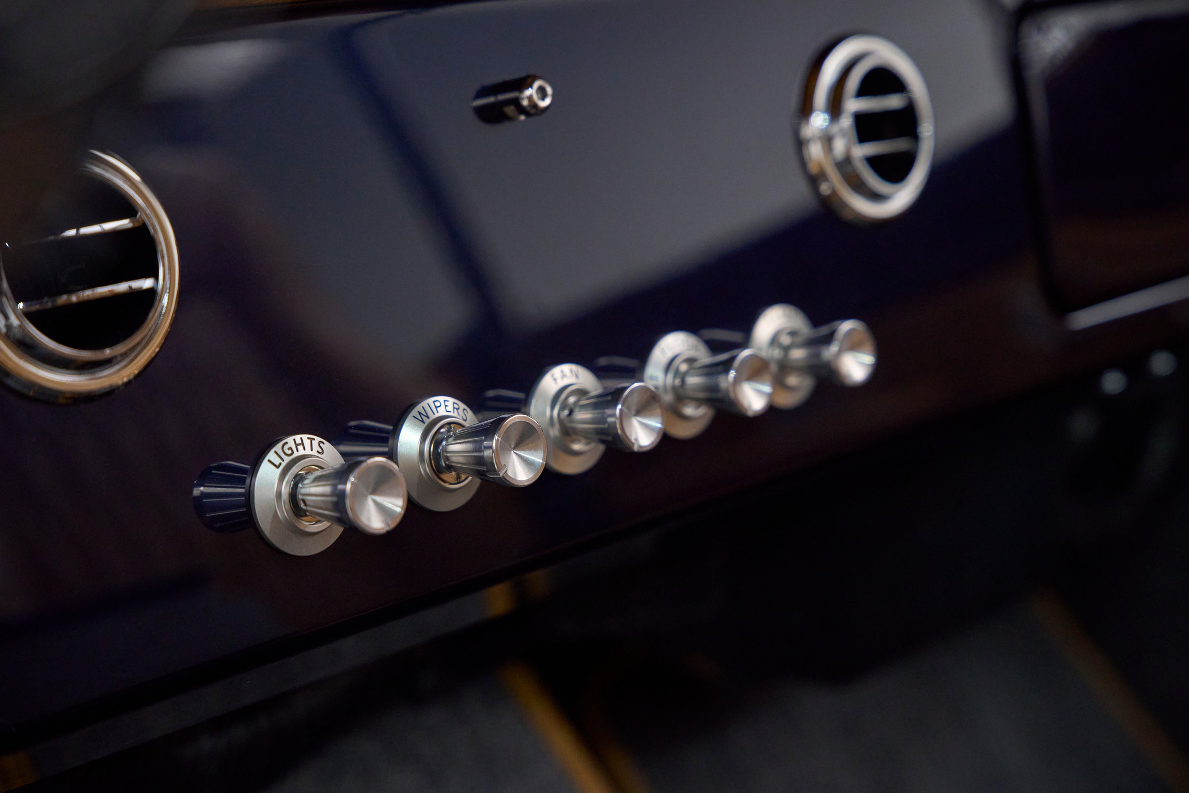 Close-up of chrome control knobs labeled lights, wipers, fan, floor, def, temp on dashboard