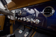 Close-up of dashboard with chrome control knobs and air vents on navy blue Classic Ford Bronco