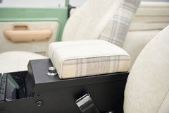 Plaid and cream armrest with seatbelt buckles beside front seats in classic Ford Bronco.