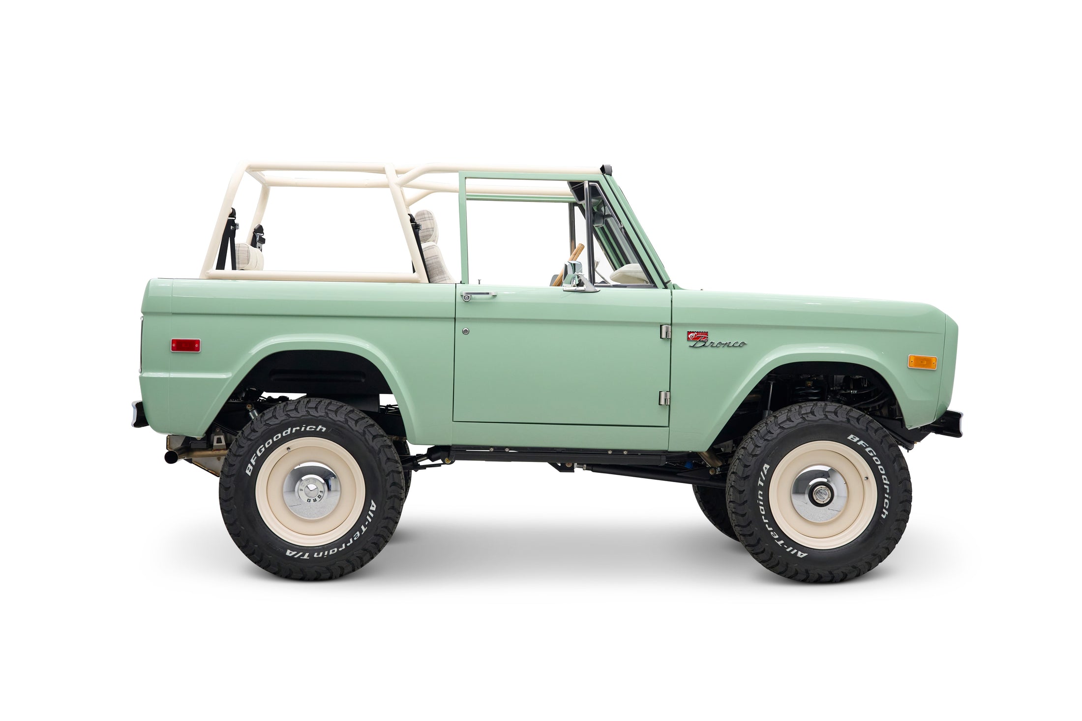 Side view of classic Ford Bronco with light green body and white roll cage.