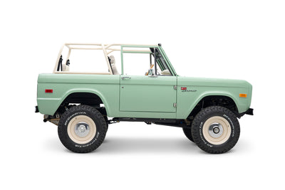 Side view of classic Ford Bronco with light green body and white roll cage.