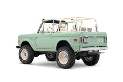 Rear three-quarter view of light green Classic Ford Bronco with white roll cage and off-road tires