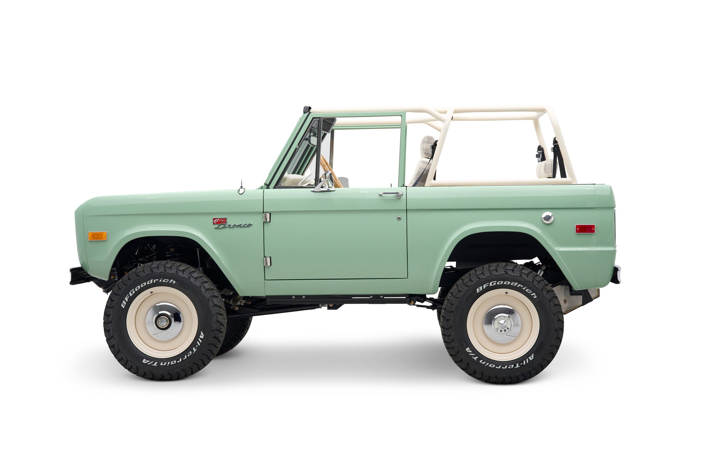 Side view of light green Classic Ford Bronco with white roll cage and off-road tires
