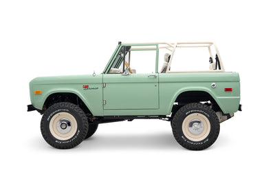 Side view of light green Classic Ford Bronco with white roll cage and off-road tires