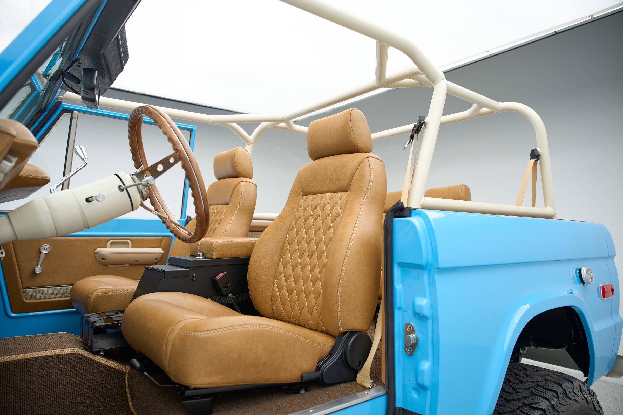 Interior view of a Classic Ford Bronco showing tan leather seats and door panel with roll cage