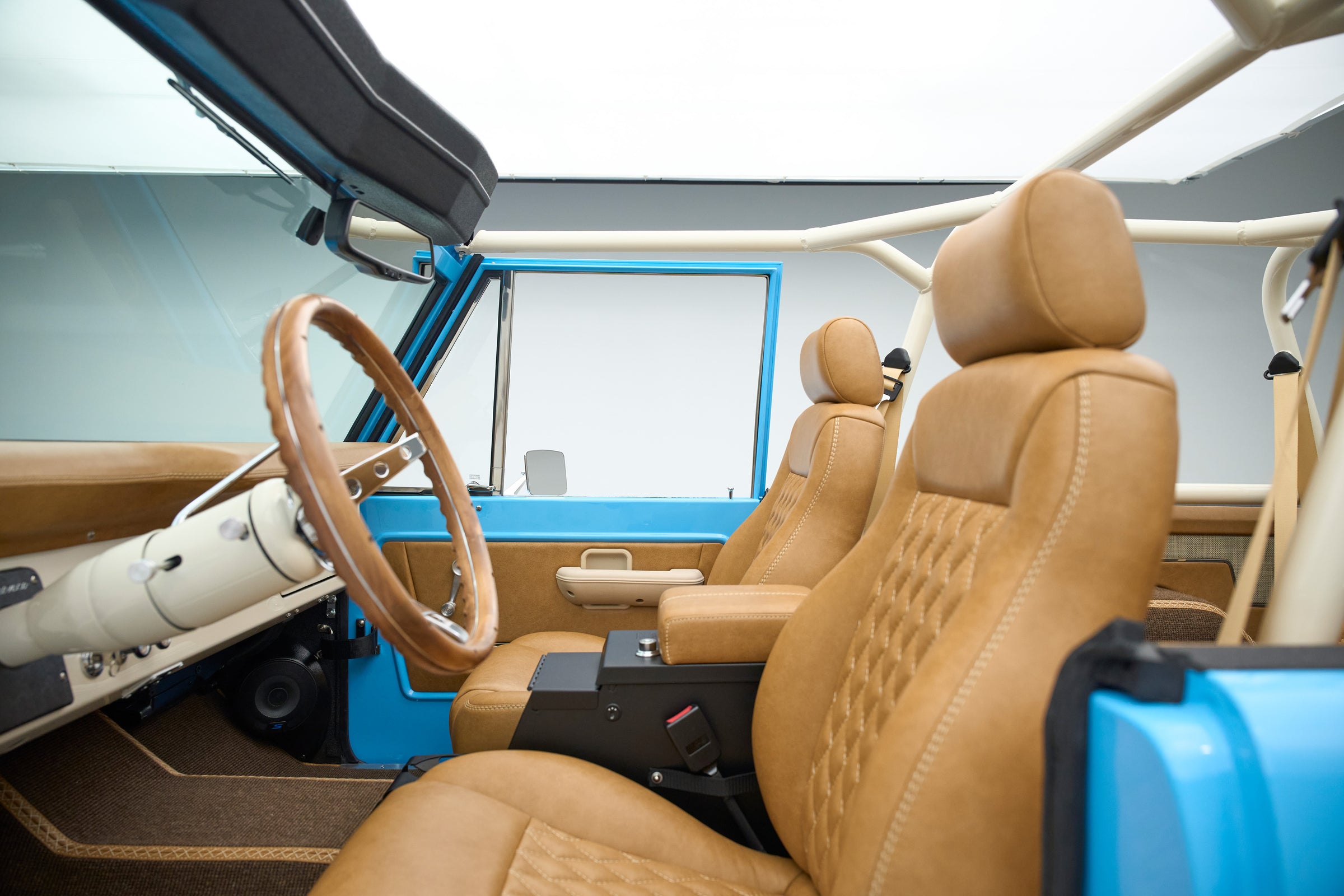 Driver and passenger seats of a Classic Ford Bronco with brown leather upholstery and roll cage