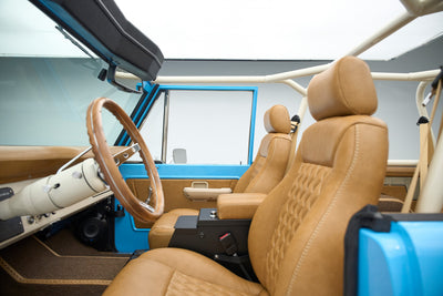 Driver and passenger seats of a Classic Ford Bronco with brown leather upholstery and roll cage