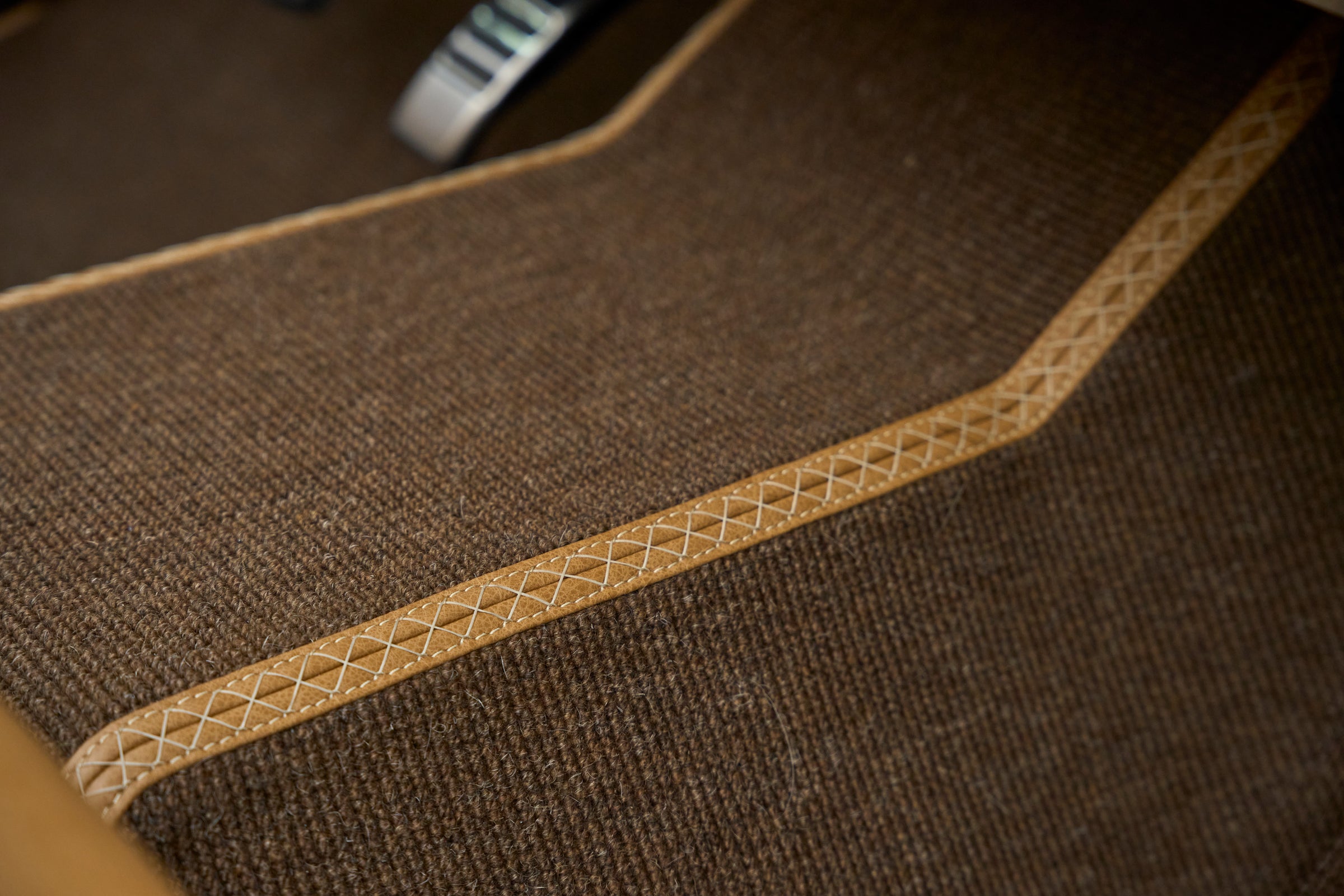 Brown carpet floor mat with stitched tan leather trim detail in vehicle interior