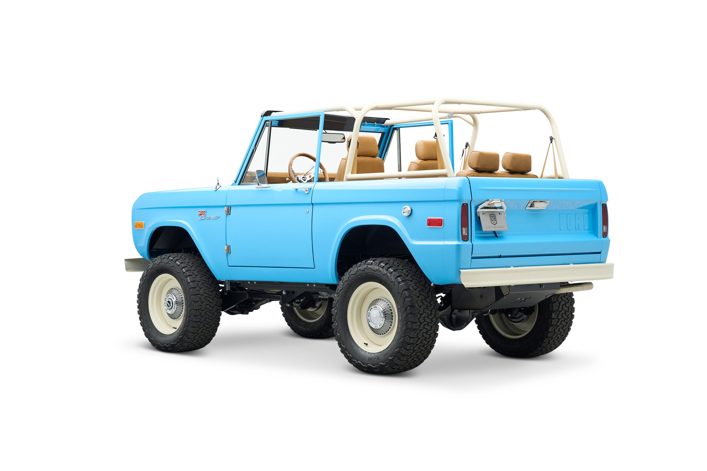 Side rear angle view of light blue Classic Ford Bronco with beige roll cage and seats