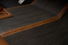 Detail of dark textured fabric upholstery with brown leather trim and cross-stitching