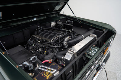 Engine bay of a Classic Ford Bronco showing detailed engine components and battery