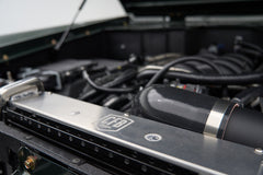 Close-up of a radiator support with 'CFB' badge and black intake hose in a Classic Ford Bronco