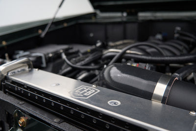 Close-up of a radiator support with 'CFB' badge and black intake hose in a Classic Ford Bronco