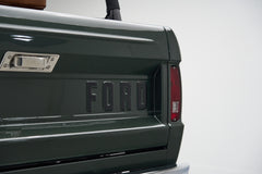 Rear tailgate with raised 'FORD' lettering and taillight on a green Classic Ford Bronco
