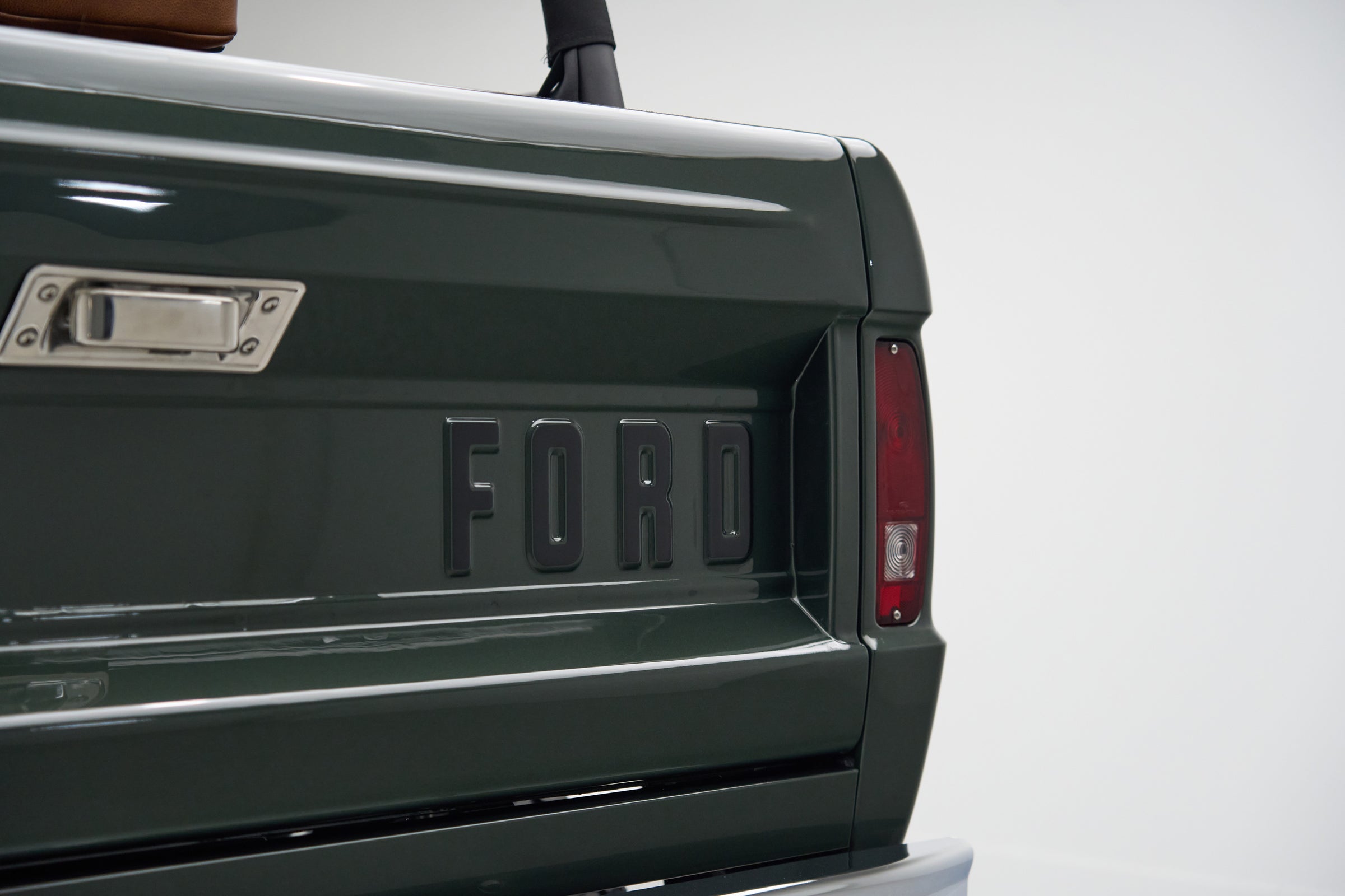 Rear tailgate with raised 'FORD' lettering and taillight on a green Classic Ford Bronco