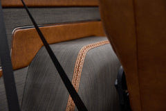 Close-up of rear seat fabric and tan leather trim with black seatbelt inside vehicle